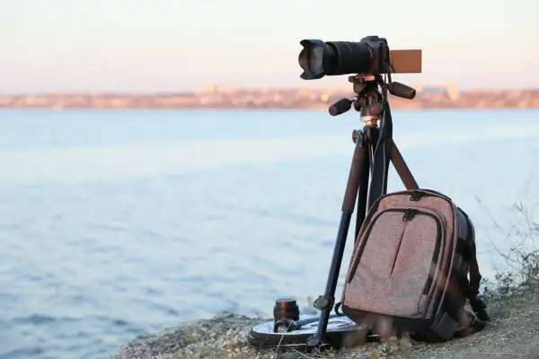 Equipo de fotografia basica listo para capturar el paisaje: cámara en trípode, mochila y lente junto al mar.