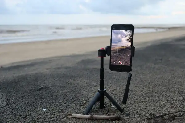 Un tripode casero sostiene un teléfono móvil en la playa, listo para grabar el mar y el cielo.