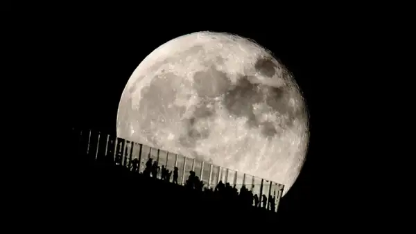 Siluetas de personas observan la luna llena desde una pasarela de cristal. Los parámetros de la foto de la luna capturan su textura y brillo.