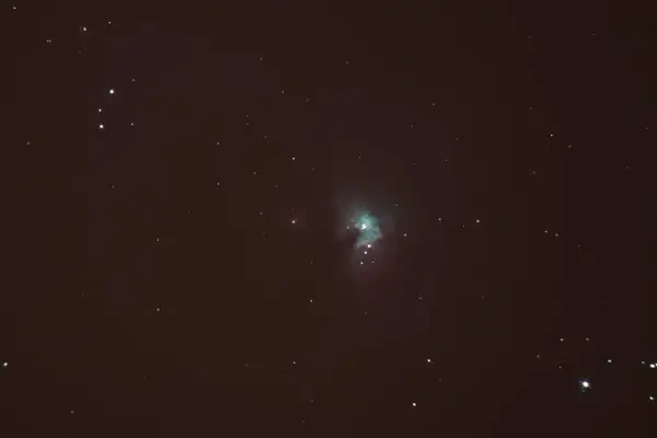 Nebulosa verdosa en el cielo nocturno, rodeada de estrellas y con tenues estelas de estrellas.